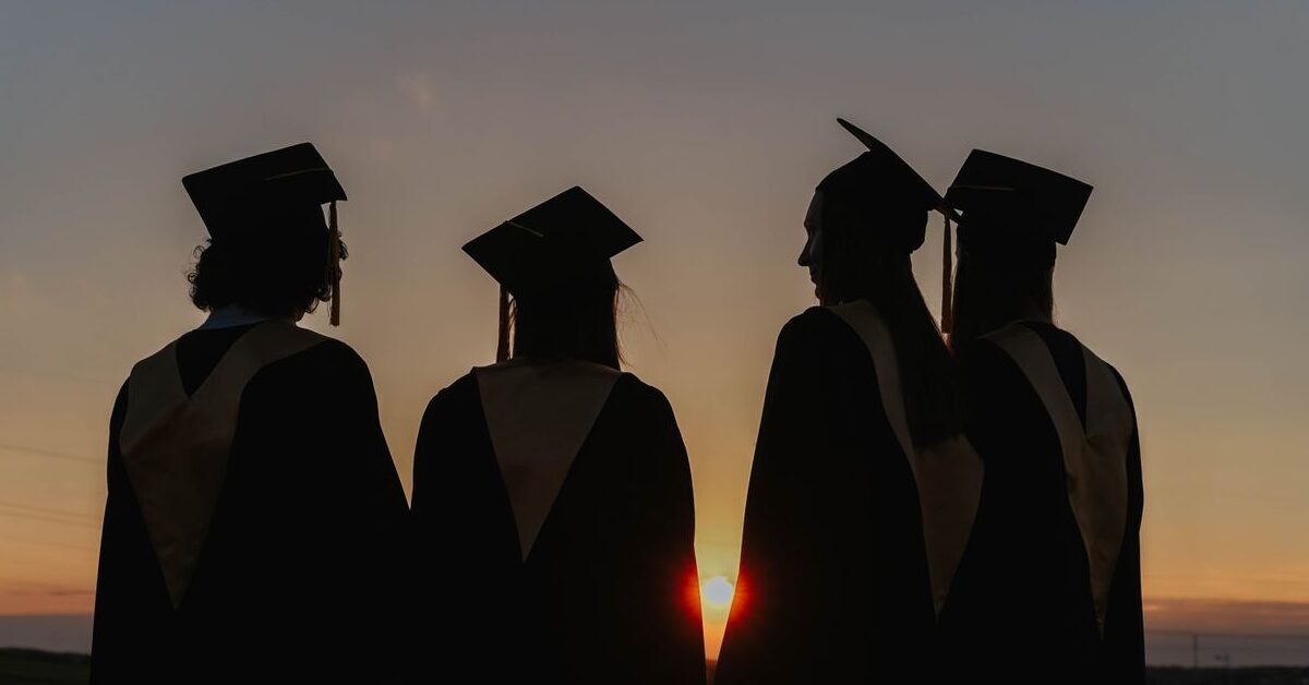 A group of graduates in caps and gowns silhouetted against a beautiful sunset, symbolizing achievement.