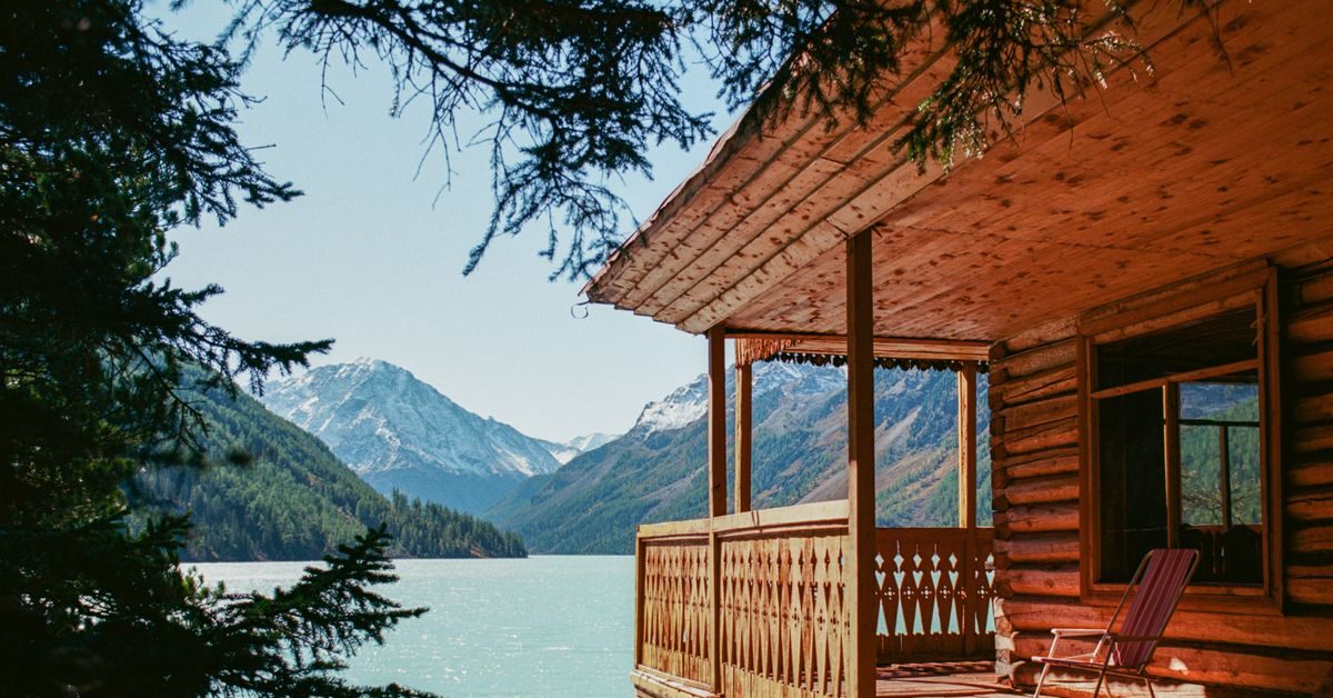Tranquil scene of a wooden cabin overlooking a serene mountain lake, surrounded by lush forest.