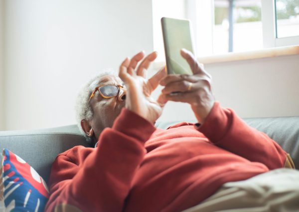 Elderly man relaxing on couch, engaging with his smartphone indoors.