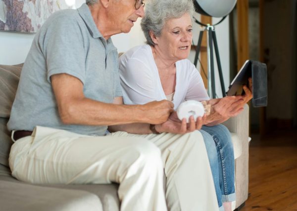 Elderly couple enjoying leisure time indoors using a tablet on a comfortable sofa.